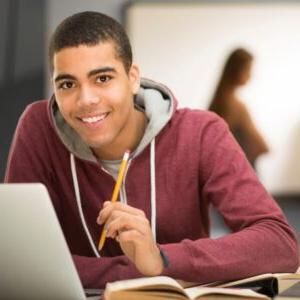 带着笔记本电脑的微笑学生坐在桌子旁 & 拿着铅笔的书